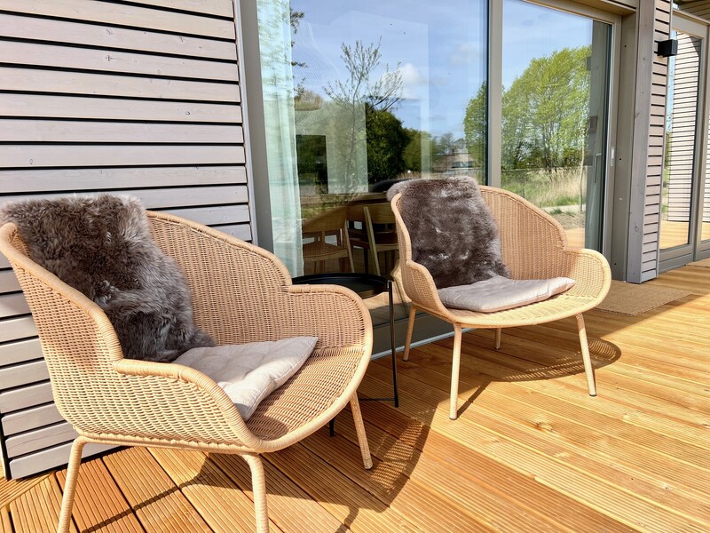 Terrasse vom Haus NordseeZeit mit zwei Rattansesseln, Fellen, Beistelltisch und Fensterfront in der Sonne
