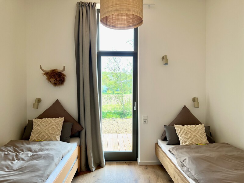 Schlafzimmer im Haus NordseeZeit mit zwei Einzelbetten, Wandleuchten und Terrassentür mit Naturblick