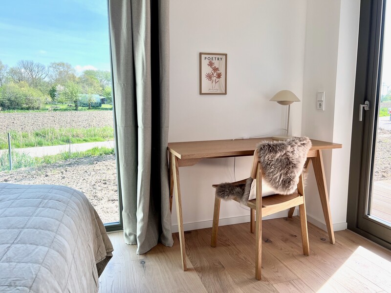 Schreibtisch aus Holz mit Stuhl und Leuchte im Haus NordseeZeit am Fenster mit Blick ins Grüne