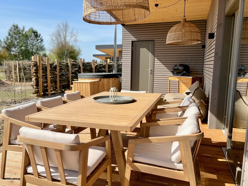Terrasse vom Haus NordseeZeit mit Holz-Sitzgruppe, Rattan-Pendelleuchten, Grill und Hot Tub im Sonnenlicht
