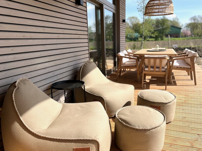 Terrasse vom Haus NordseeZeit mit beigen Sitzsäcken, Hockern, Esstisch und Rattanleuchte mit Feldblick