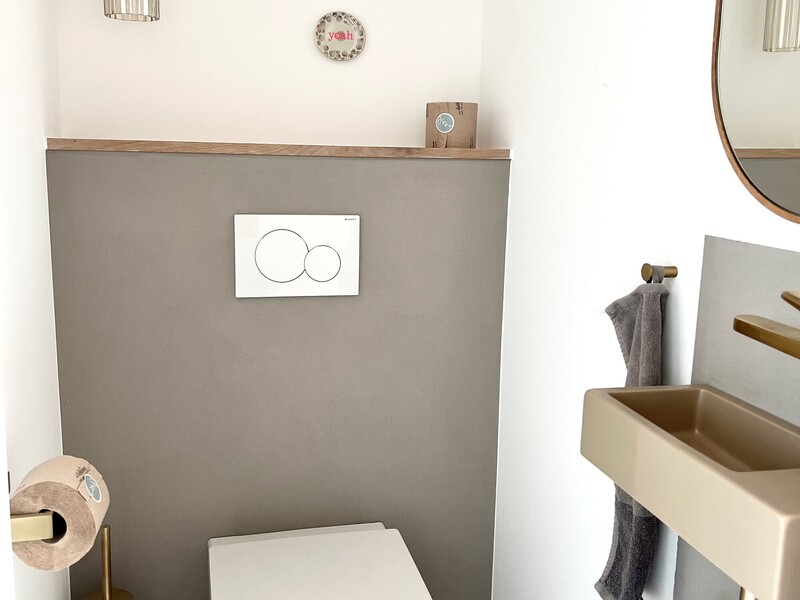 Gäste-WC im Haus NordseeZeit mit Wand-WC, Betonwaschbecken, goldenen Armaturen und grauer Wand