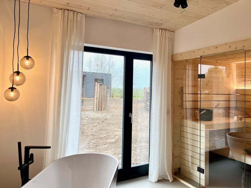 Badezimmer im StrandHaus mit freistehender Badewanne, Sauna, Pendelleuchten und Fenster ins Grüne