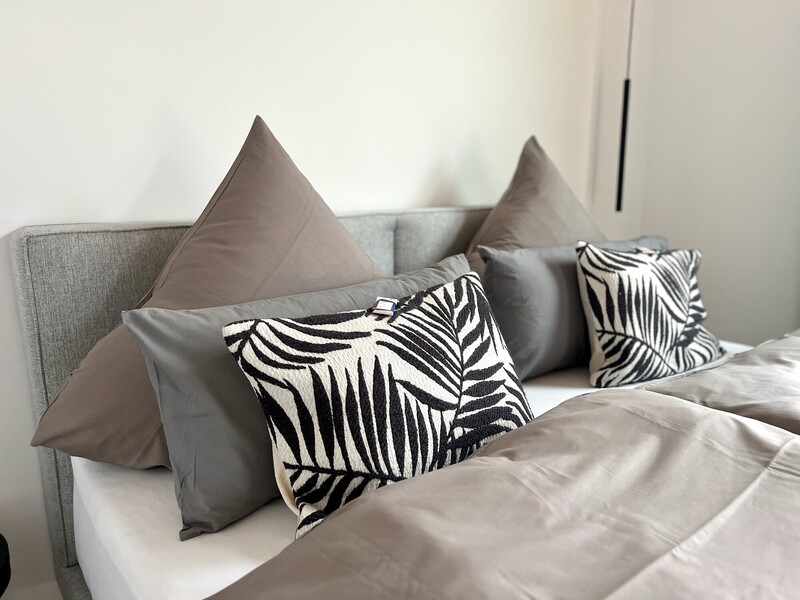 Bett-Detail im StrandHaus mit Kissen und grauem Polster-Kopfteil