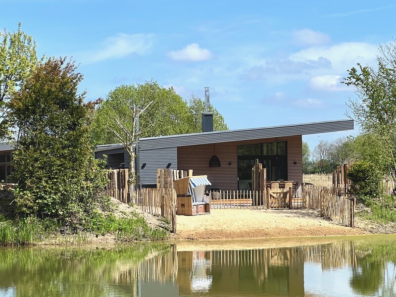 Außenansicht vom StrandHaus: modernes Flachdachhaus mit Holzfassade, Spiegelung im Teich und Bäumen