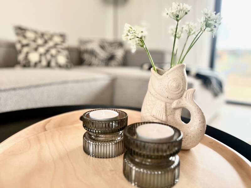 Deko-Detail im StrandHaus: fischförmige Vase mit weißen Blüten und Teelichthalter auf Holztisch