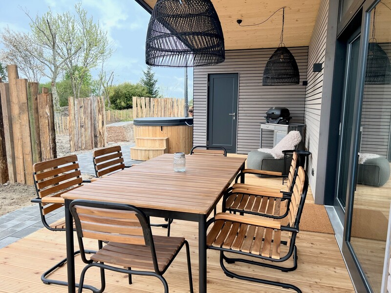Überdachte Terrasse vom StrandHaus mit Holz-Esstisch, schwarzen Stühlen, Rattanleuchte und Badebottich