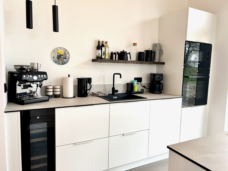 Küchenzeile im StrandHaus mit weißen Fronten, Espressomaschine, schwarzen Regalen und Einbaugeräten