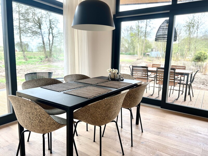 Essbereich im StrandHaus mit schwarzem Esstisch, Rattanstühlen und großer Fensterfront zur Terrasse