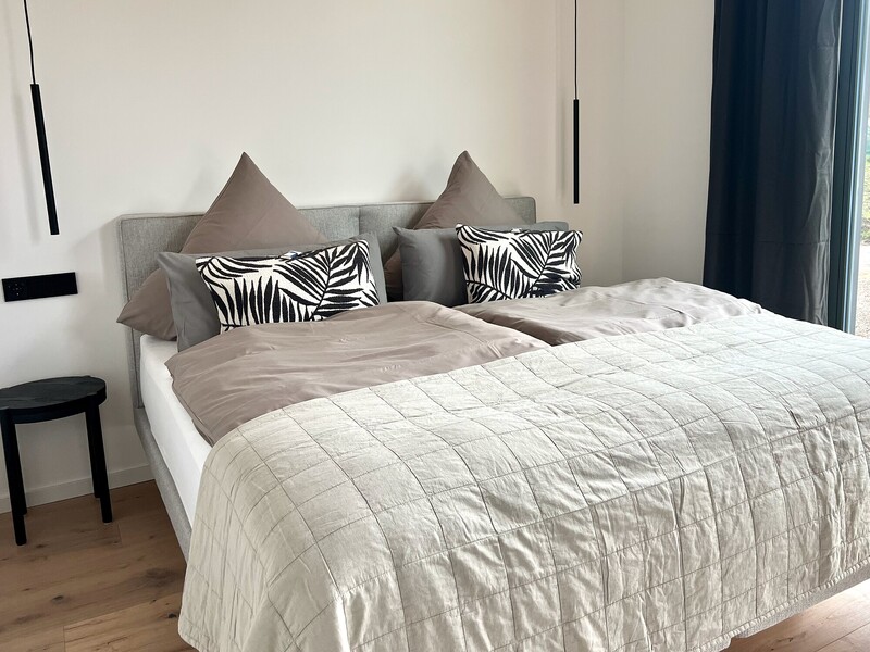 Elternschlafzimmer im StrandHaus mit Boxspringbett, grauen und schwarz-weißen Kissen und Hocker