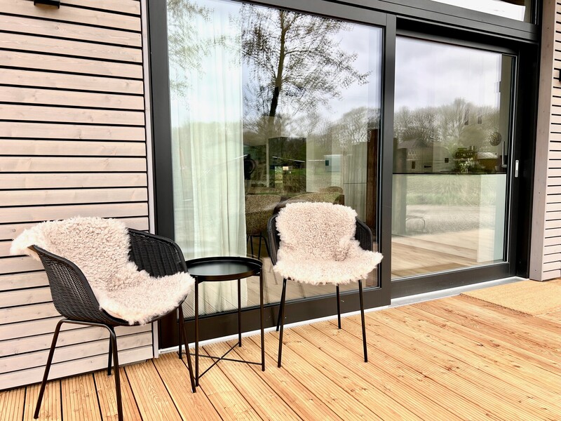 Terrasse vom StrandHaus mit zwei Stühlen mit Fellauflagen, Beistelltisch und Fensterfront