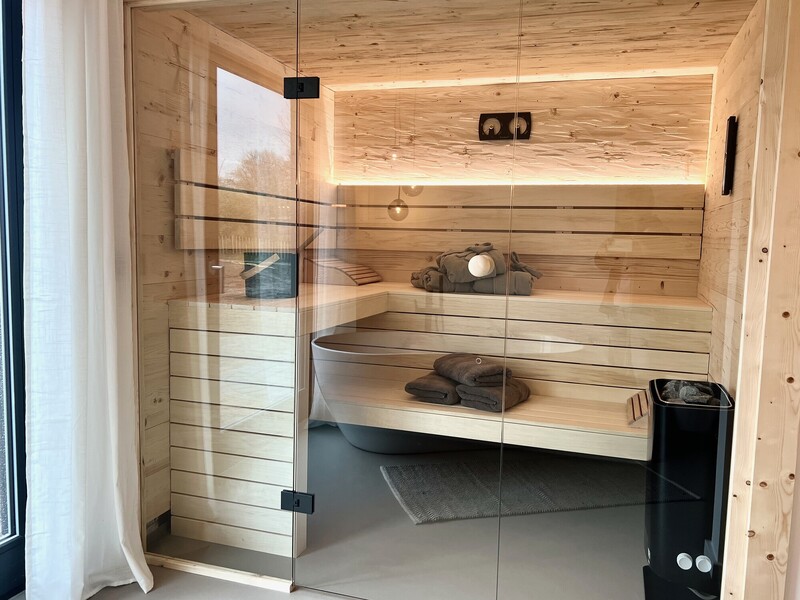 Sauna im StrandHaus mit Holzbänken, Saunaofen und Glasfront mit indirekter Beleuchtung