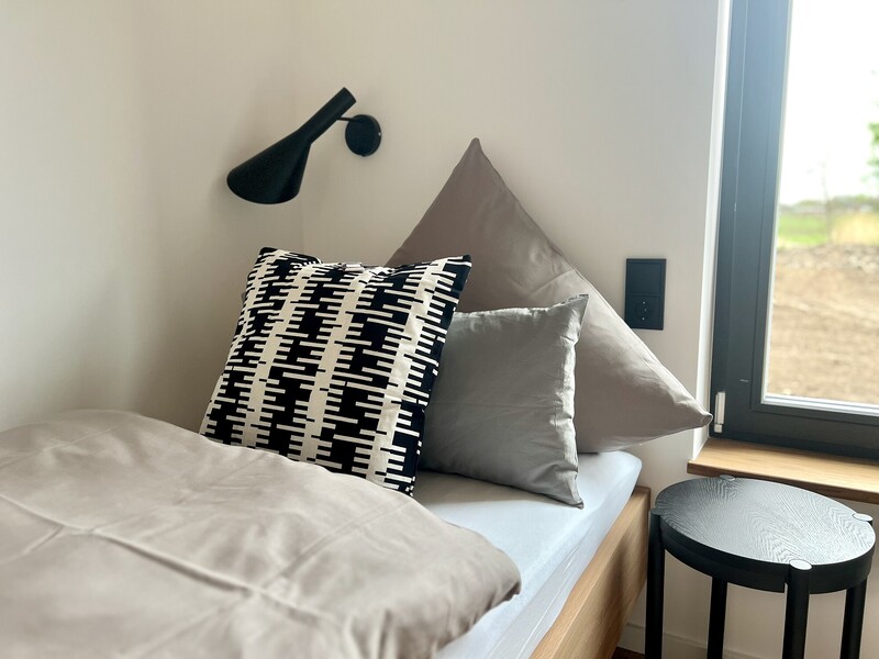 Kinderschlafzimmer von StrandHaus mit Einzelbett, grauen und schwarz-weißen Kissen, Wandleuchte und Hocker