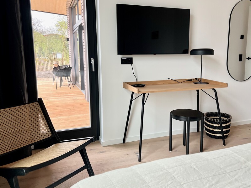 Arbeitsecke im Schlafzimmer im StrandHaus mit Holzschreibtisch, Stuhl, Fernseher und Terrassentür