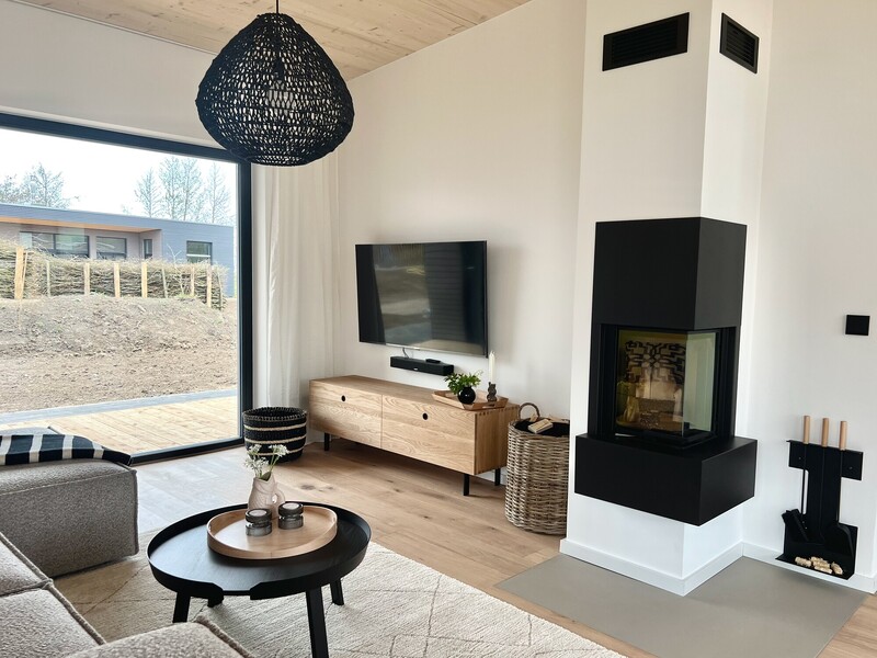 Wohnzimmer im StrandHaus mit Kaminofen, Fernseher, Sideboard und schwarzer Rattan-Pendelleuchte