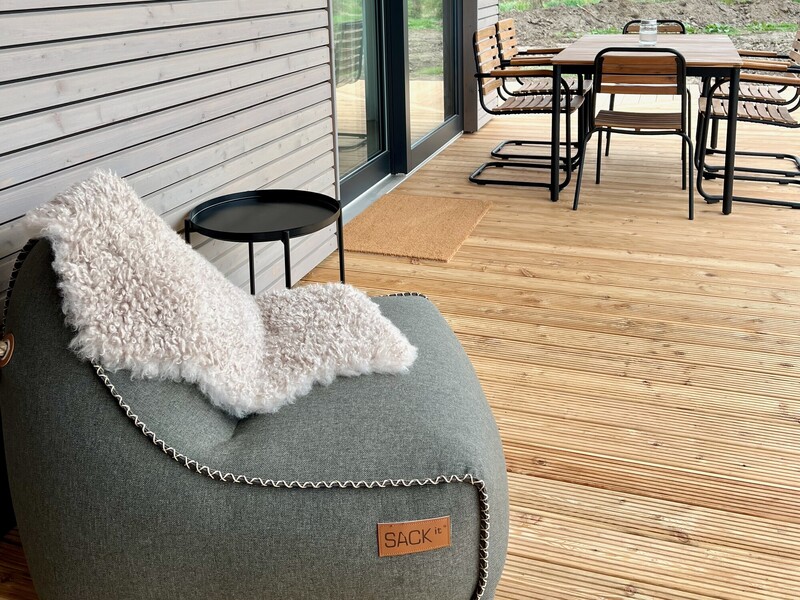 Terrasse vom StrandHaus mit grauem Sitzsack, Fellauflage und Esstisch im Hintergrund