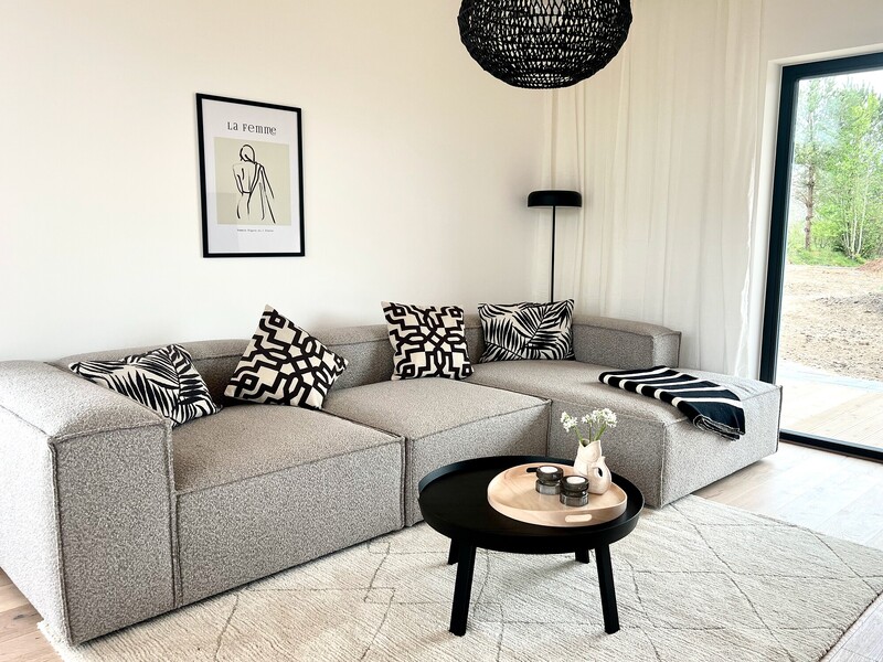 Wohnzimmer vom StrandHaus mit grauem Ecksofa, schwarz-weißen Kissen und rundem Couchtisch