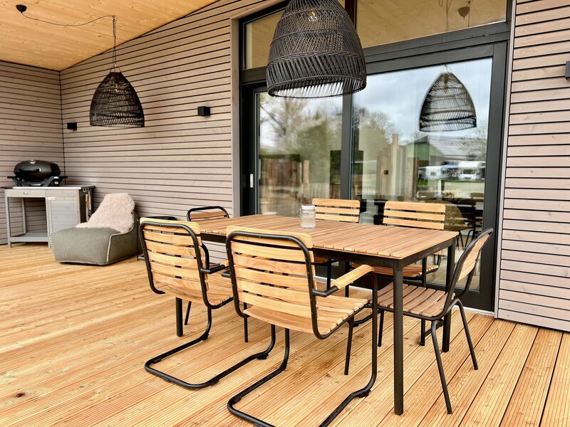Überdachte Terrasse vom StrandHaus mit Holz-Esstisch, schwarzen Stühlen, Rattanleuchten und Grill