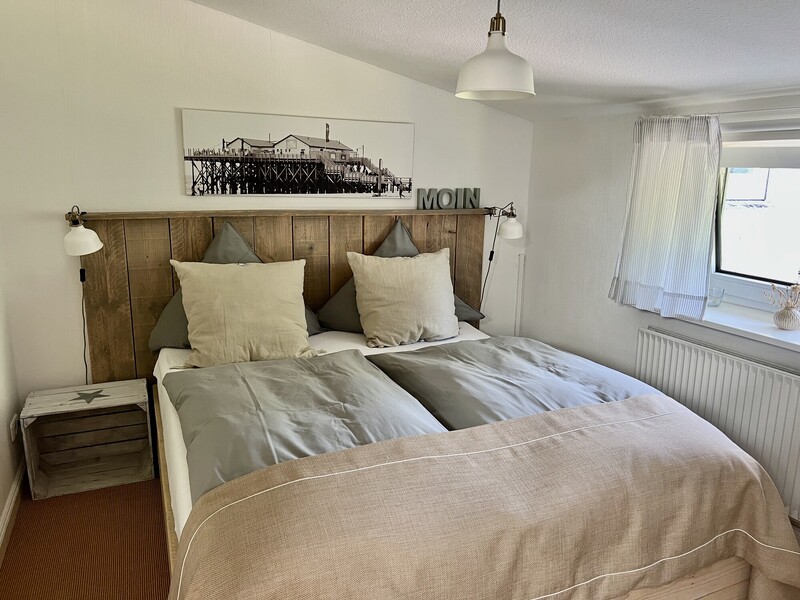 Schlafzimmer mit Doppelbett, Holzkopfteil und Nordsee-Deko („MOIN