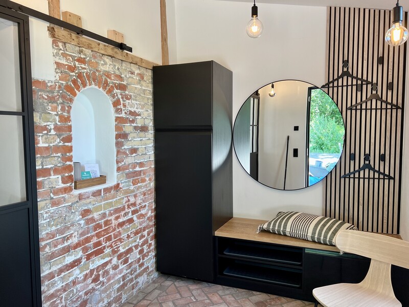 Eingangsbereich im Industrial-Stil mit Ziegelwand und Nische, schwarzem Kühlschrank, Sitzbank mit Stauraum, rundem Spiegel und Garderobenleiste