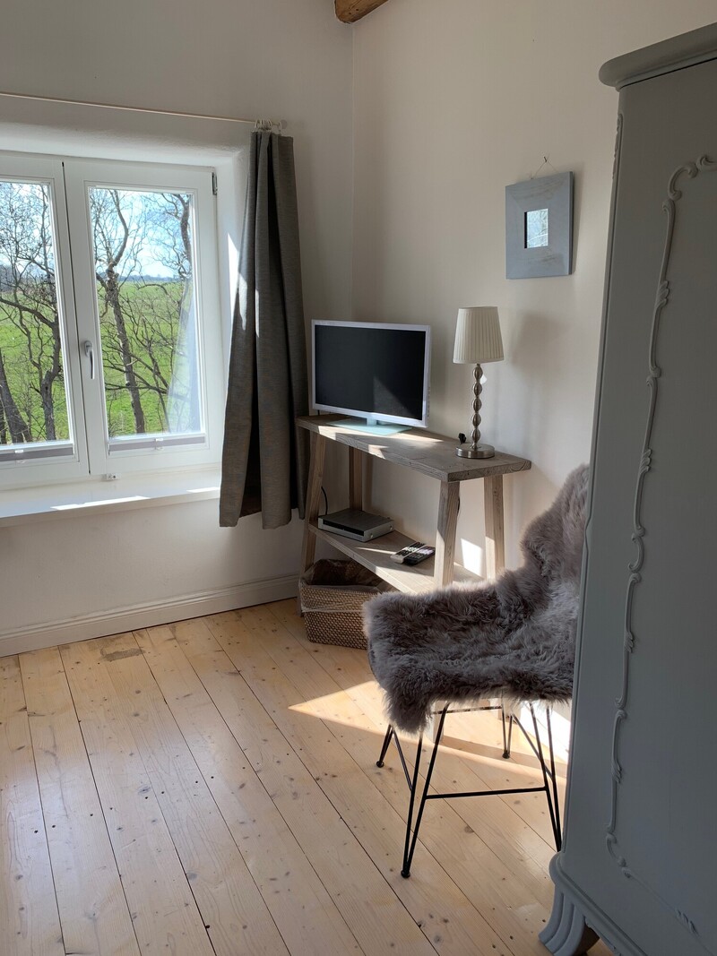Zimmerecke einer Ferienunterkunft mit Fernseher, Fellsessel und Fenster mit Blick über die Felder