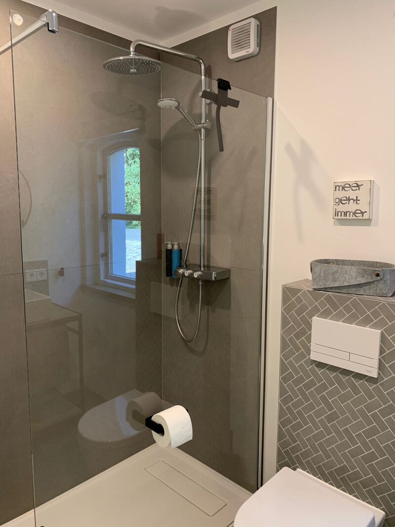 Badezimmer im Haus NordseeStil mit ebenerdiger Dusche, Regenduschkopf, Glaswand, WC und grauen Fliesen