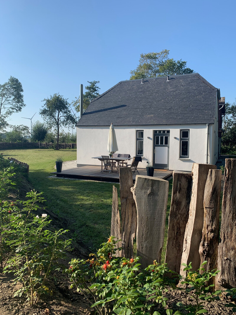 Außenansicht vom Haus NordseeStil mit Terrasse, Gartentisch, Sonnenschirm und Grünflächen bei blauem Himmel