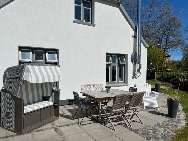 Terrasse vom Haus NordseeStil mit Strandkorb, Holztisch mit Stühlen und weißer Hausfassade bei Sonnenschein