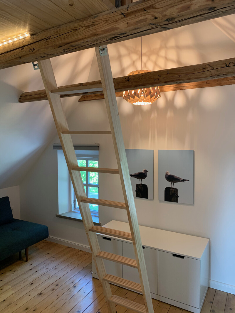 Dachzimmer im Haus NordseeStil mit Holzleiter zum Hochbett, Holzbalken, Sofa, Sideboard und Möwenbildern