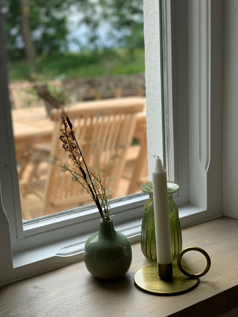 Fensterbank im Haus NordseeStil mit Vasen und Kerzenständer, Blick auf Terrasse mit Gartenmöbeln