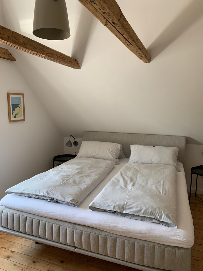 Schlafzimmer unterm Dach im Haus NordseeStil mit Boxspringbett, Holzbalken, Dachschräge und Dielenboden