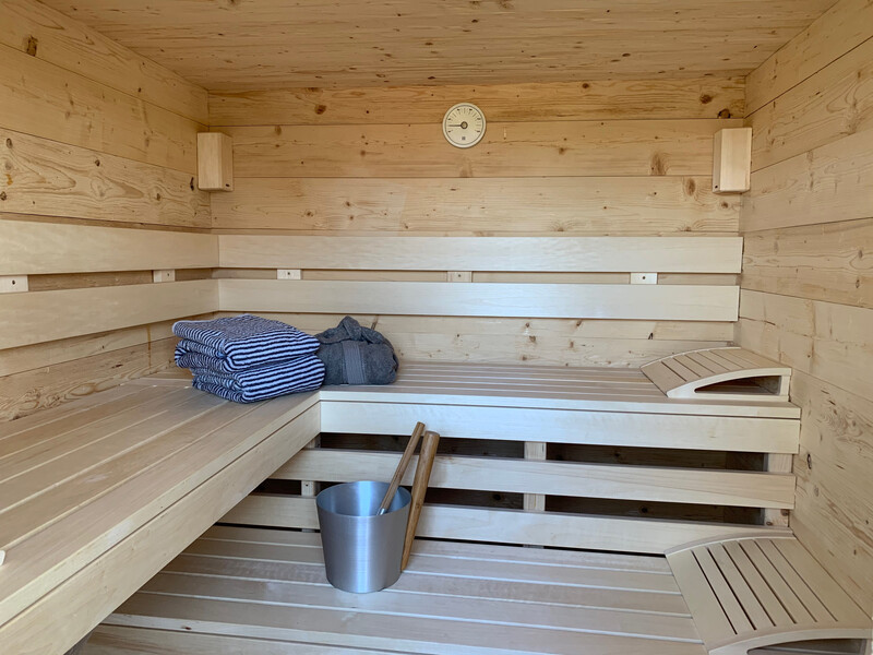 Sauna im Haus NordseeStil mit Holzbänken, Handtüchern, Aufgusskübel und Sanduhr an der Wand