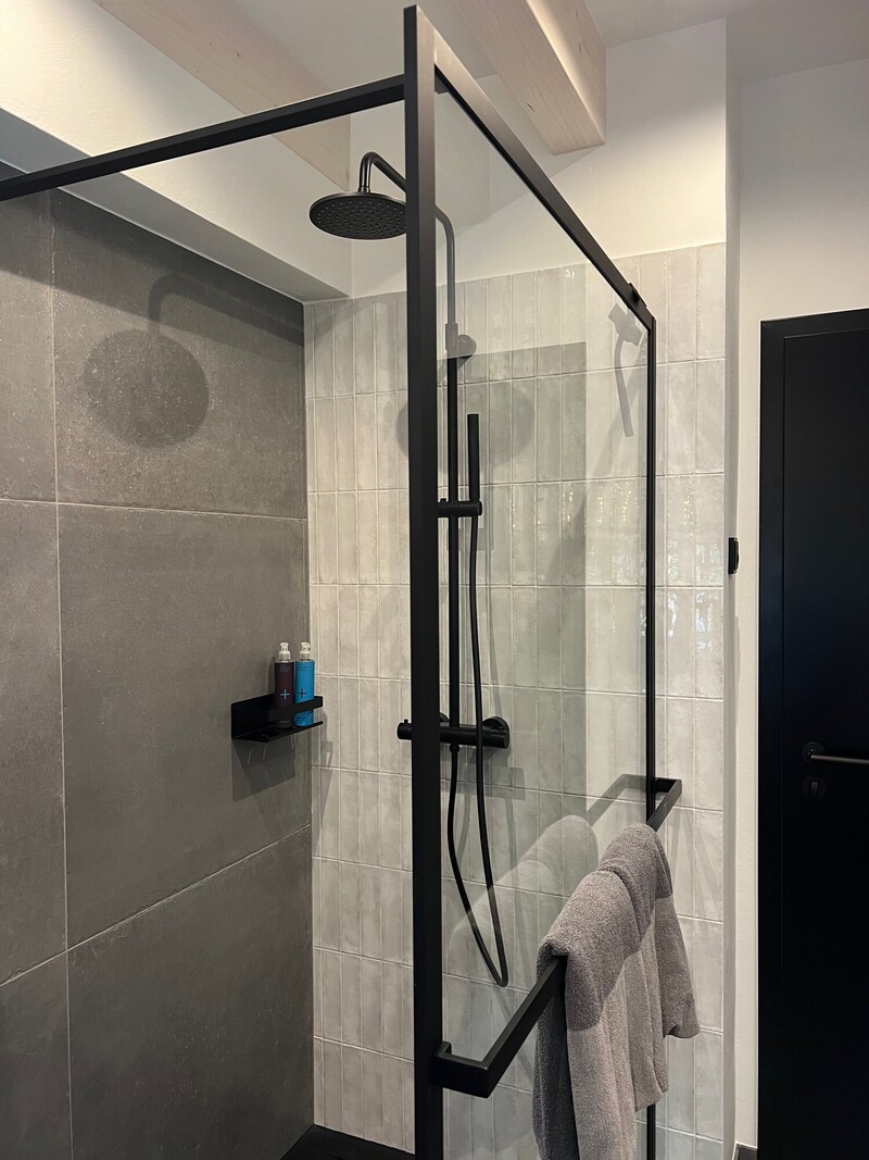 Ebenerdige Dusche im Haus Scheune mit schwarzem Regenduschkopf, Glaswand, Handtuchhalter und grauen Fliesen