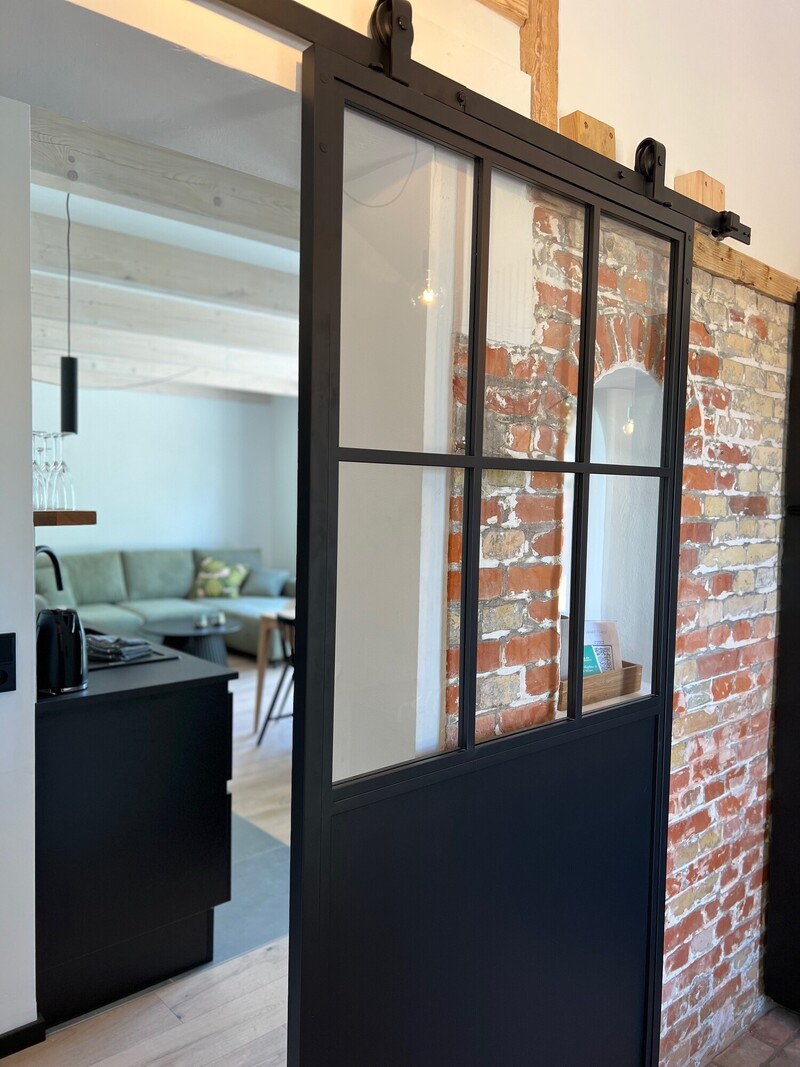 Haus Scheune mit schwarzer Glas-Schiebetür im Loft-Stil, Backsteinwand und Blick in den Wohnbereich