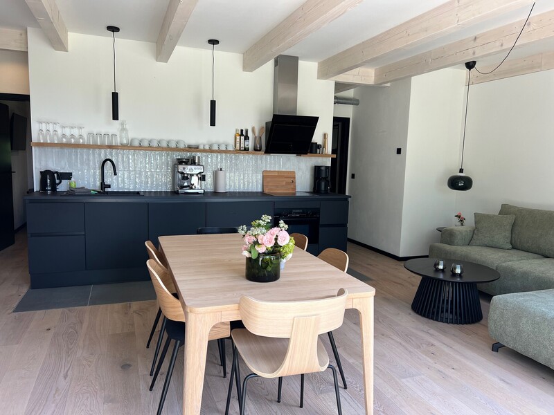 Offener Wohn-Essbereich im Haus Scheune mit schwarzer Küche, Holzesstisch, grünem Sofa und Holzbalken