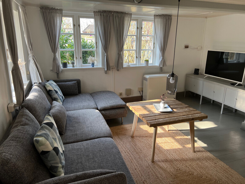 Wohnzimmer der Reetdachkate 1813 mit grauem Ecksofa, Holzcouchtisch, Flachbild-TV und Sprossenfenstern