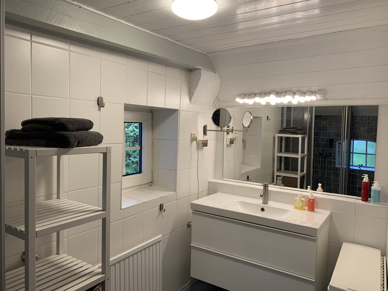 Badezimmer der Reetdachkate 1813 mit Waschtisch, großem Spiegel, Handtuchregal, Fenster und weißen Fliesen