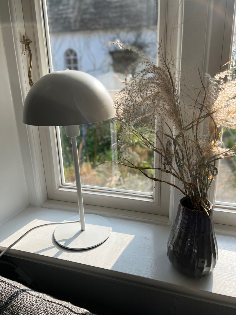 Fensterbank der Reetdachkate 1813 mit Tischlampe, Vase mit Trockengräsern und Blick in den Garten