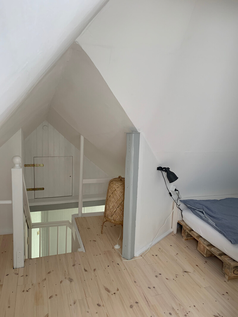 Dachzimmer der Reetdachkate 1813 mit Palettenbett, Dachschräge, Treppenaufgang und Dielenboden